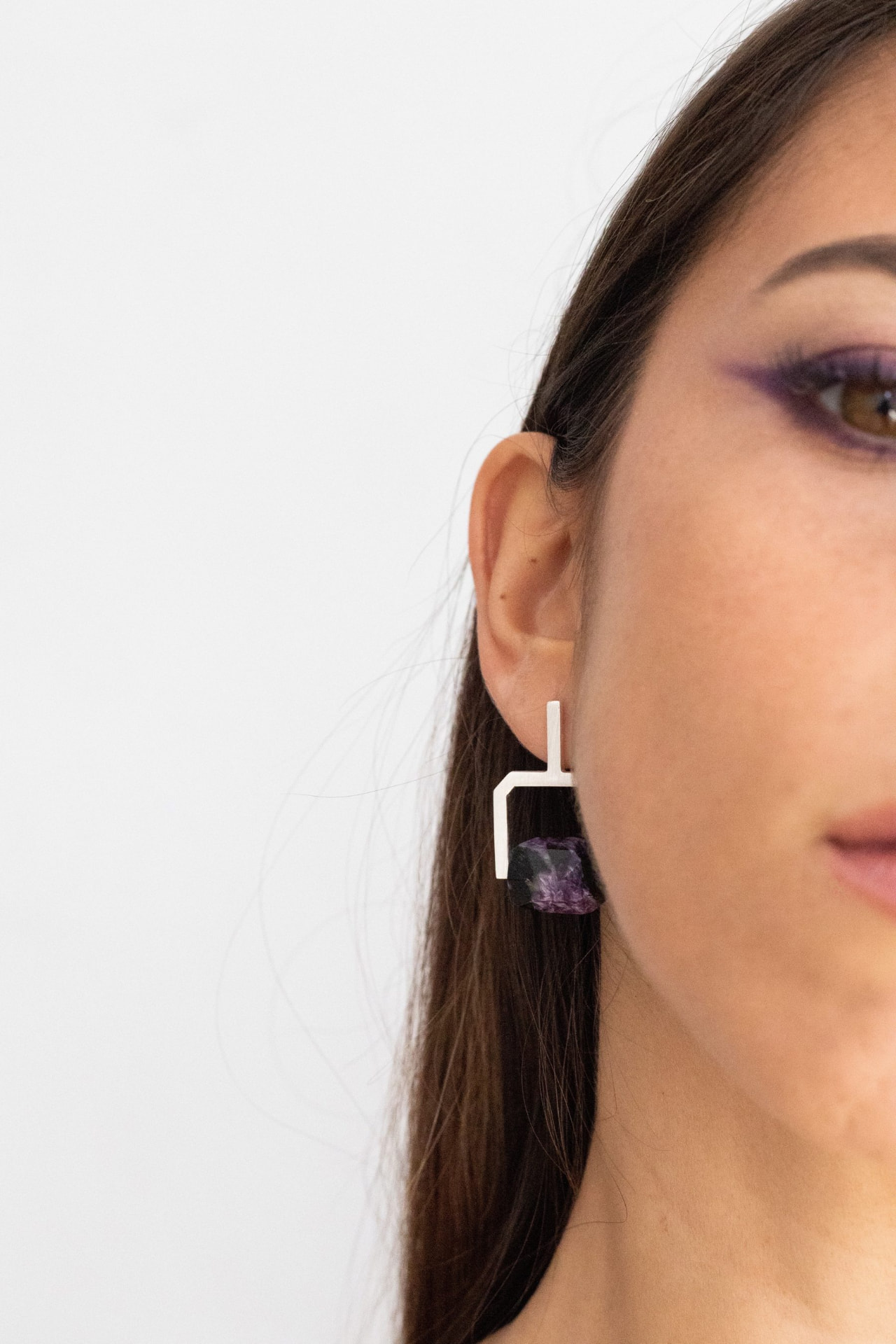 Primer plano de perfil con eyeliner gráfico en violeta y un pendiente de diseño dorado