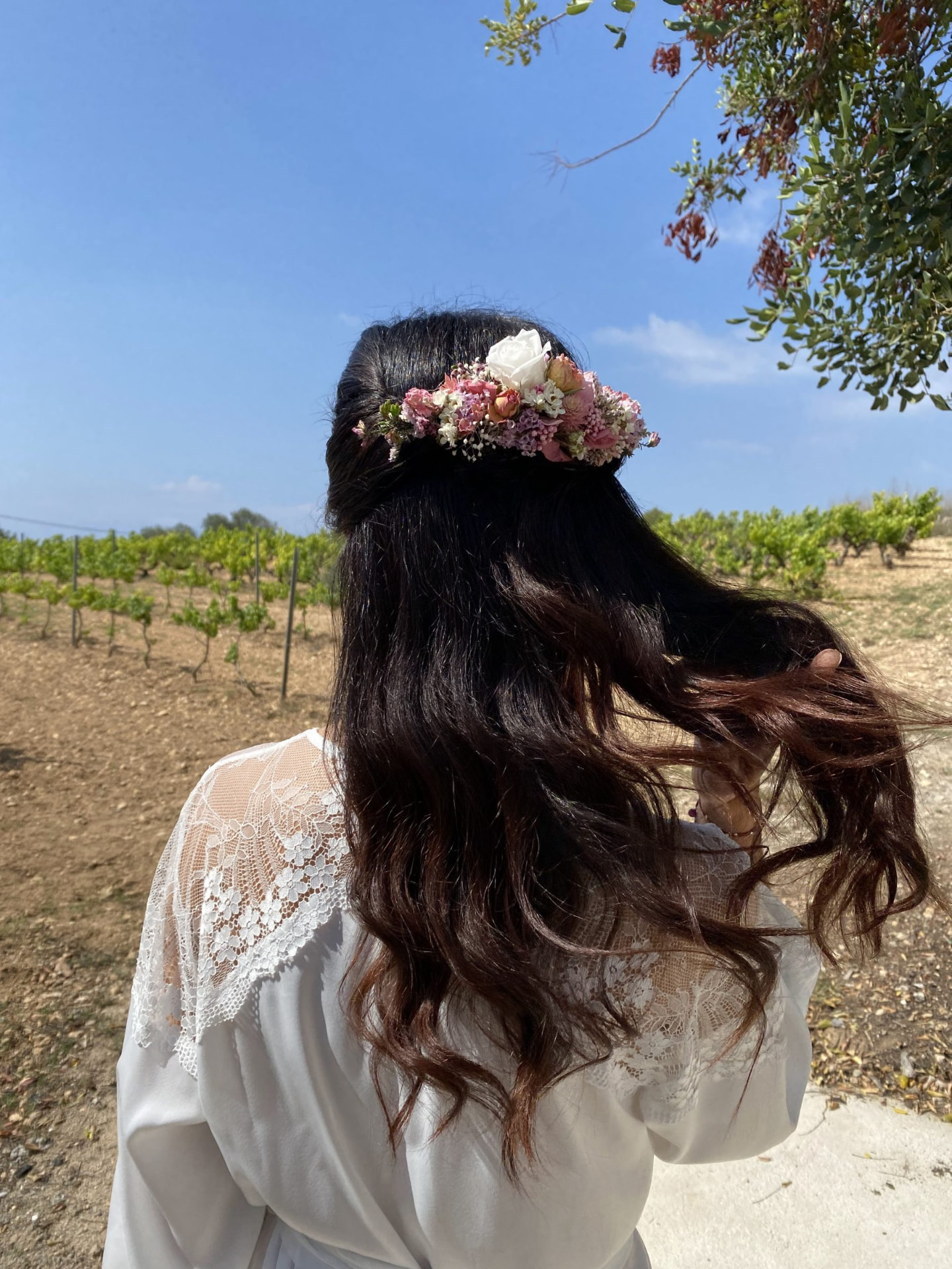 Corona de flores naturales sobre un peinado semirrecogido de novia en un viñedo, con piel iluminada y labios nude